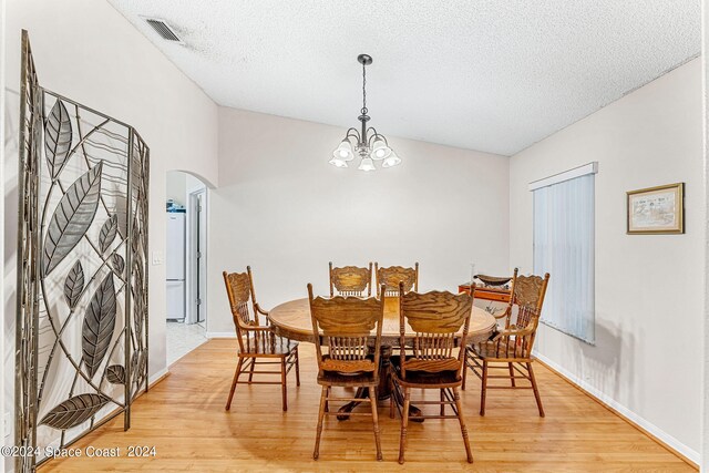 dining space featuring lofted ceiling, an inviting chandelier, a textured ceiling, and light hardwood / wood-style flooring