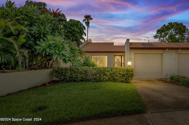 view of front of property featuring stucco siding, a garage, a yard, and driveway