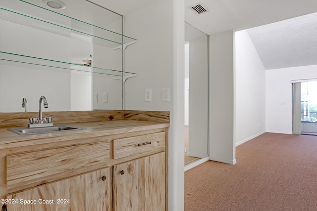 kitchen with a textured ceiling, carpet, sink, and light brown cabinetry