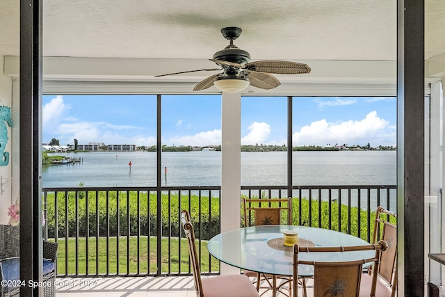 sunroom with ceiling fan and a water view