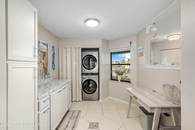 laundry room featuring stacked washing maching and dryer, light tile patterned flooring, and a textured ceiling