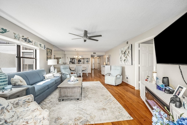 living room featuring a textured ceiling, ceiling fan with notable chandelier, and wood-type flooring