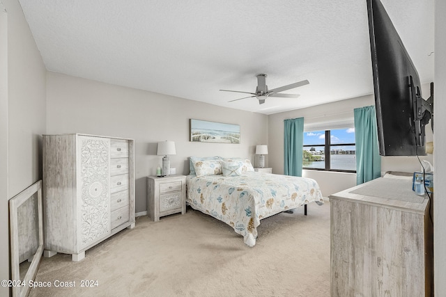 bedroom with a textured ceiling, light colored carpet, and ceiling fan