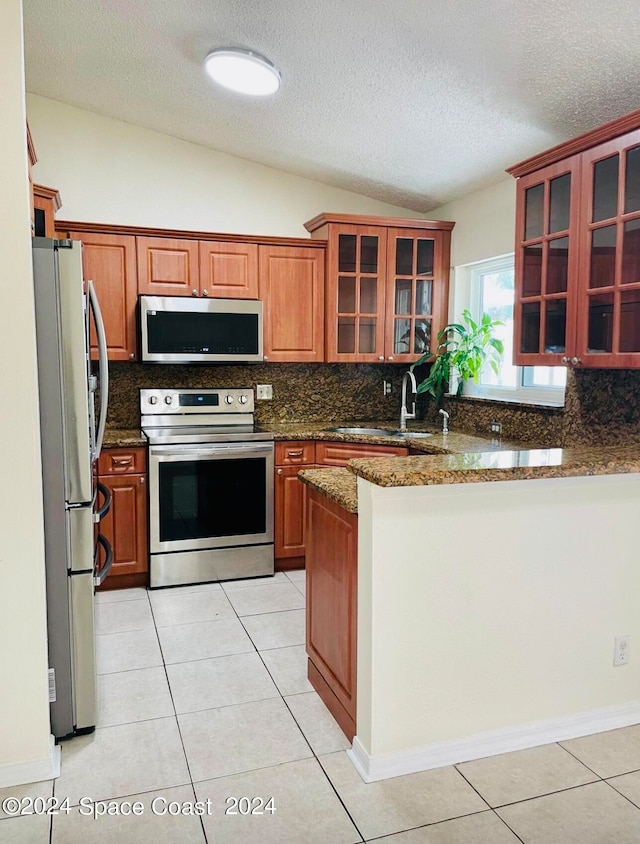 kitchen featuring stainless steel appliances, kitchen peninsula, lofted ceiling, stone counters, and light tile patterned flooring