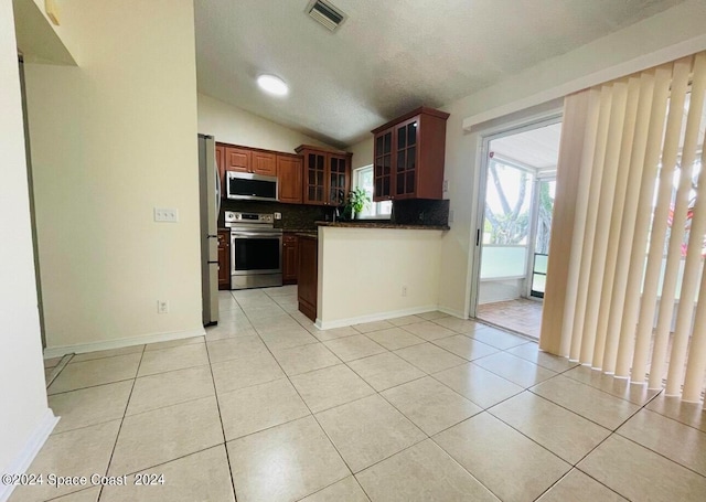 kitchen featuring appliances with stainless steel finishes, vaulted ceiling, light tile patterned floors, and a textured ceiling