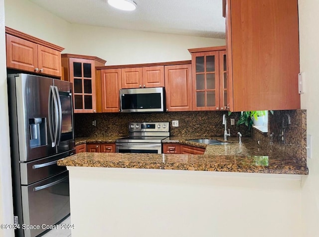 kitchen with dark stone countertops, appliances with stainless steel finishes, sink, lofted ceiling, and tasteful backsplash