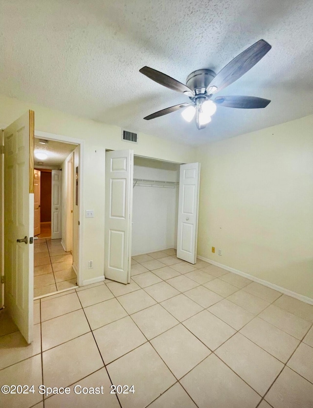 unfurnished bedroom featuring a textured ceiling, light tile patterned flooring, ceiling fan, and a closet