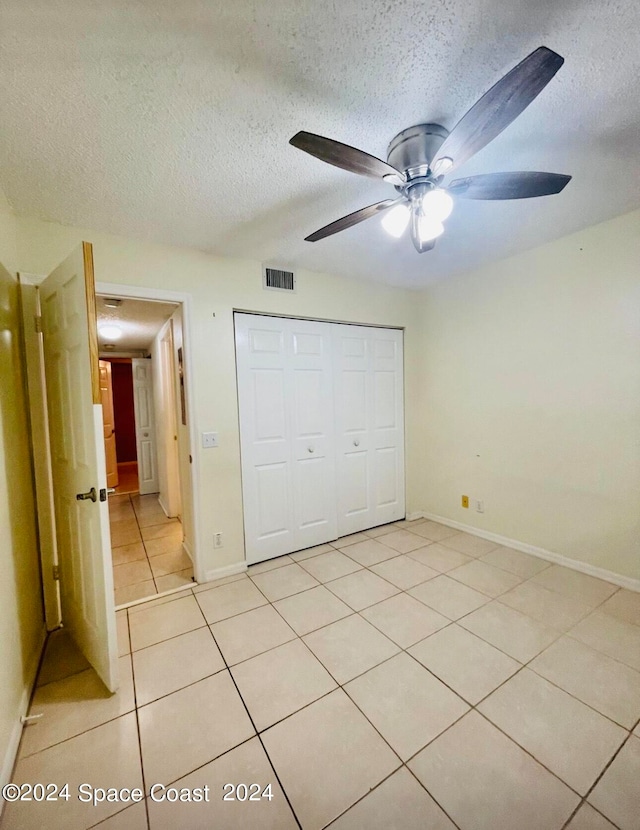 unfurnished bedroom featuring a textured ceiling, ceiling fan, light tile patterned floors, and a closet