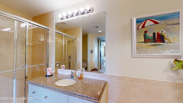 bathroom featuring a shower with door, vanity, toilet, and tile walls