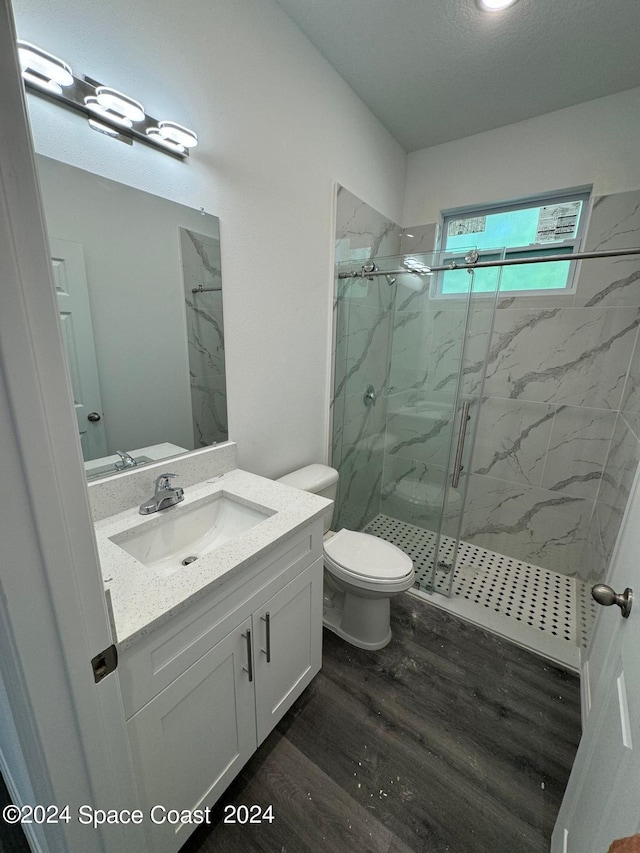 full bathroom featuring toilet, vanity, a marble finish shower, and wood finished floors