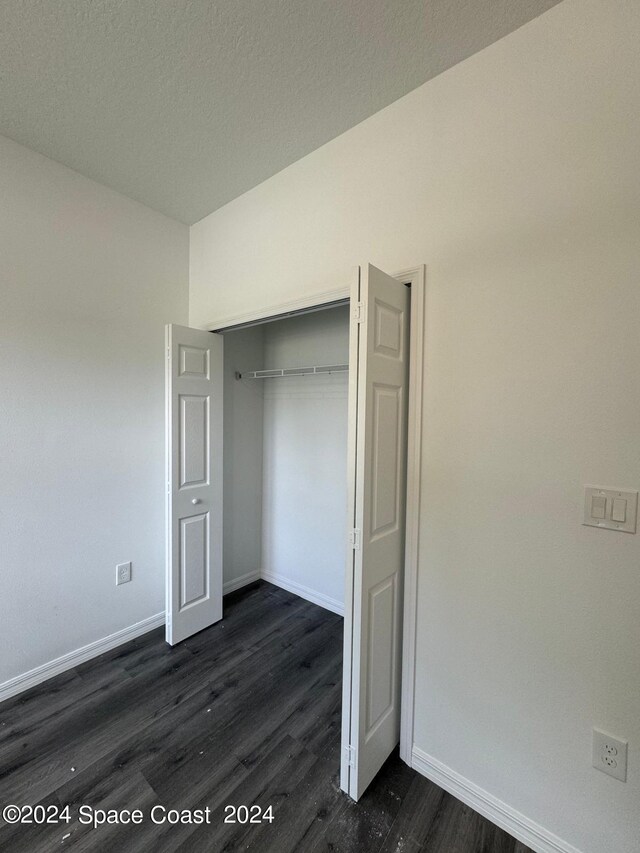 unfurnished bedroom with a textured ceiling, a closet, and dark hardwood / wood-style flooring