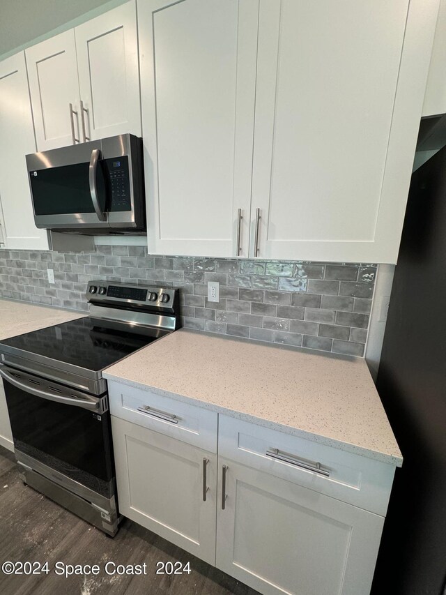 kitchen with backsplash, appliances with stainless steel finishes, dark wood-type flooring, light stone counters, and white cabinets