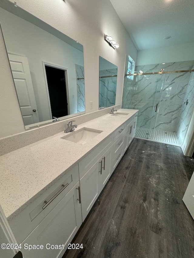bathroom featuring double vanity, a sink, a marble finish shower, and wood finished floors