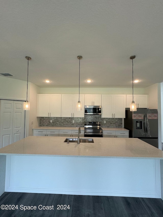 kitchen with a sink, appliances with stainless steel finishes, a center island with sink, white cabinets, and dark wood-type flooring