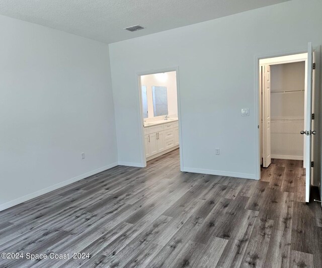 unfurnished bedroom featuring a textured ceiling, ensuite bath, a walk in closet, and hardwood / wood-style flooring