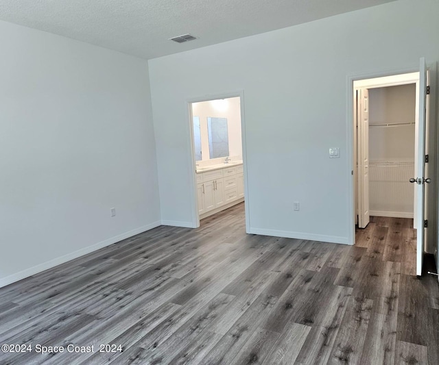 unfurnished bedroom with baseboards, a textured ceiling, wood finished floors, and a spacious closet