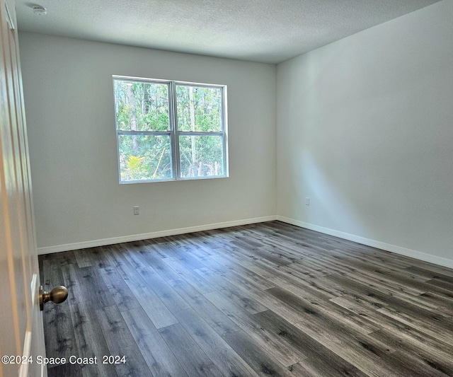 spare room with dark wood-type flooring, a textured ceiling, and baseboards