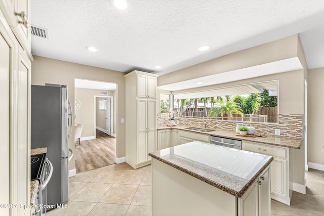 kitchen featuring light stone countertops, sink, decorative backsplash, a kitchen island, and appliances with stainless steel finishes