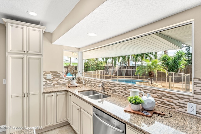 kitchen with light stone countertops, dishwasher, sink, decorative backsplash, and light tile patterned floors