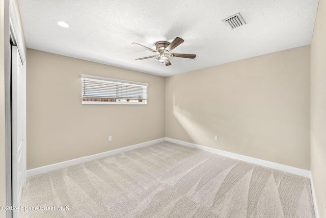 empty room featuring a textured ceiling, light colored carpet, and ceiling fan