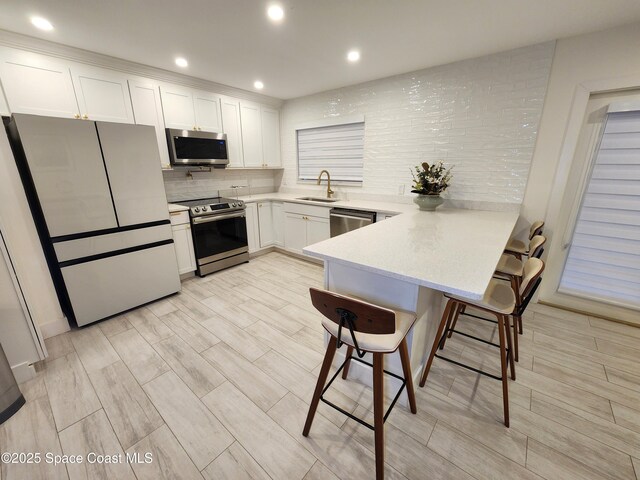 kitchen with a breakfast bar area, stainless steel appliances, a peninsula, white cabinetry, and tasteful backsplash