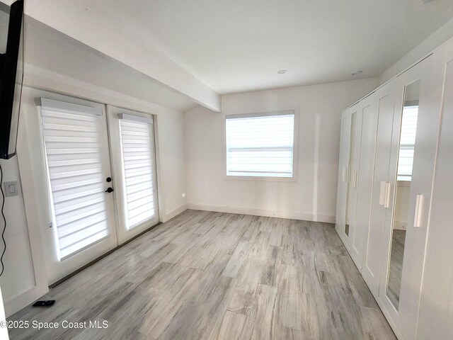 unfurnished bedroom with baseboards, french doors, lofted ceiling with beams, and light wood-style floors