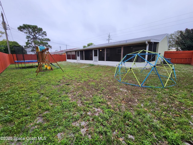 view of yard with a trampoline, a playground, a fenced backyard, and a sunroom