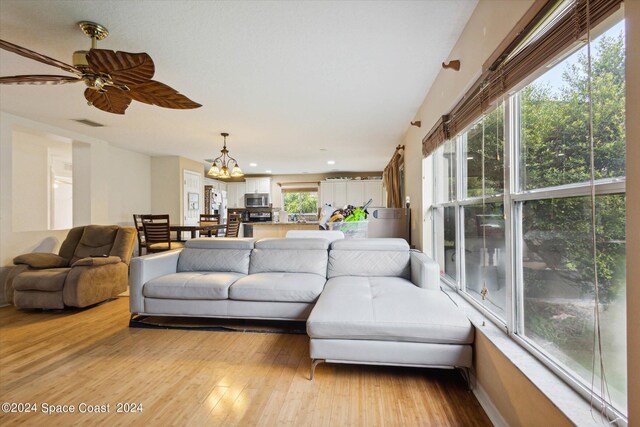 living room with ceiling fan with notable chandelier and light hardwood / wood-style flooring