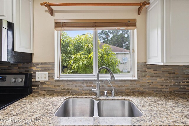 kitchen with black electric range oven, sink, light stone countertops, and white cabinets