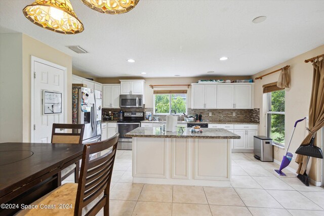 kitchen with pendant lighting, tasteful backsplash, light tile patterned floors, stainless steel appliances, and light stone counters