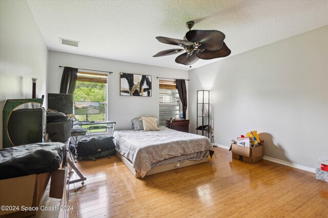 bedroom with a textured ceiling, ceiling fan, and light hardwood / wood-style floors