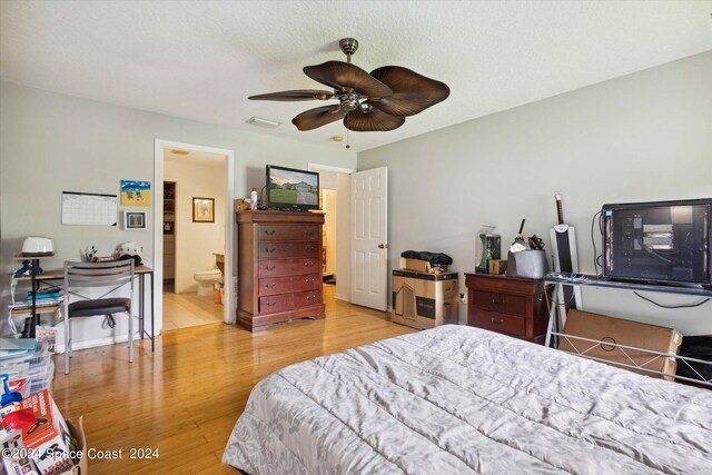 bedroom featuring light wood-type flooring, ceiling fan, ensuite bathroom, and a textured ceiling