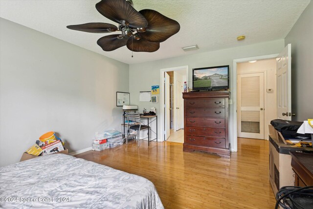 bedroom with light wood-type flooring, ceiling fan, and a textured ceiling