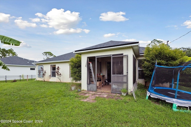 back of house featuring a trampoline, a lawn, and a sunroom