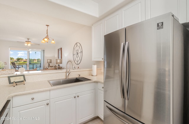 kitchen featuring sink, ceiling fan with notable chandelier, white cabinetry, pendant lighting, and stainless steel refrigerator