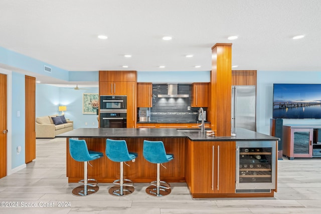 kitchen with a kitchen island with sink, light wood-type flooring, black appliances, beverage cooler, and wall chimney range hood