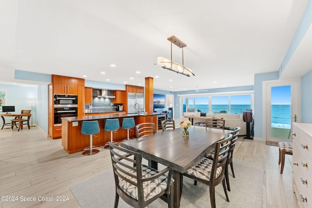 dining space with light wood-type flooring, a water view, a chandelier, and sink