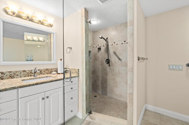 bathroom with tiled shower, tile patterned flooring, a textured ceiling, and vanity