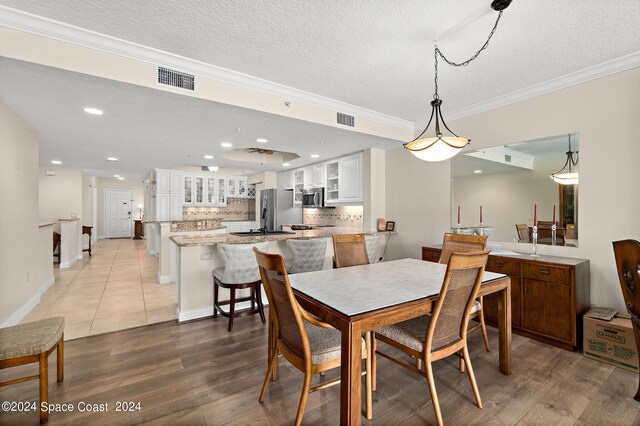 dining area with light wood-type flooring, crown molding, and a textured ceiling