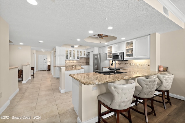 kitchen with appliances with stainless steel finishes, white cabinetry, kitchen peninsula, and a kitchen breakfast bar