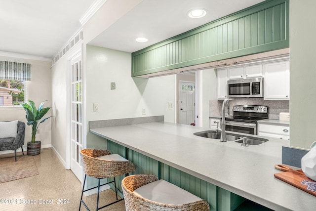 kitchen with green cabinetry, crown molding, stainless steel appliances, kitchen peninsula, and a kitchen bar