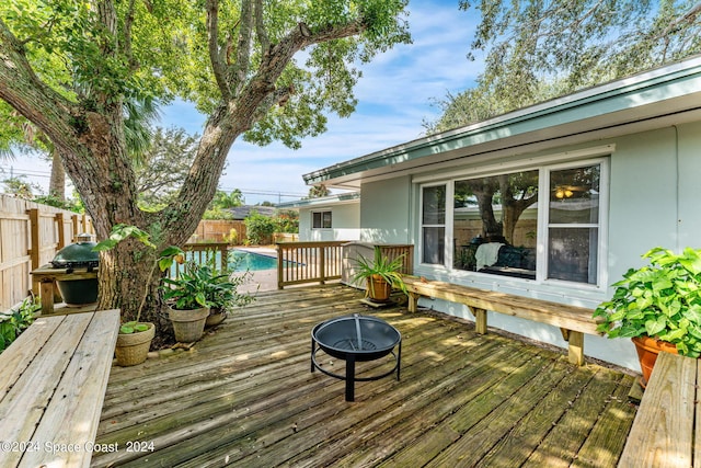 deck featuring a fenced in pool, a fire pit, and a grill