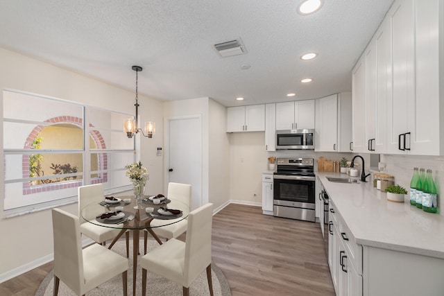 kitchen featuring light wood-type flooring, pendant lighting, stainless steel appliances, sink, and white cabinets