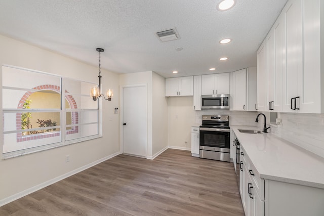 kitchen with appliances with stainless steel finishes, light hardwood / wood-style floors, white cabinetry, sink, and a textured ceiling