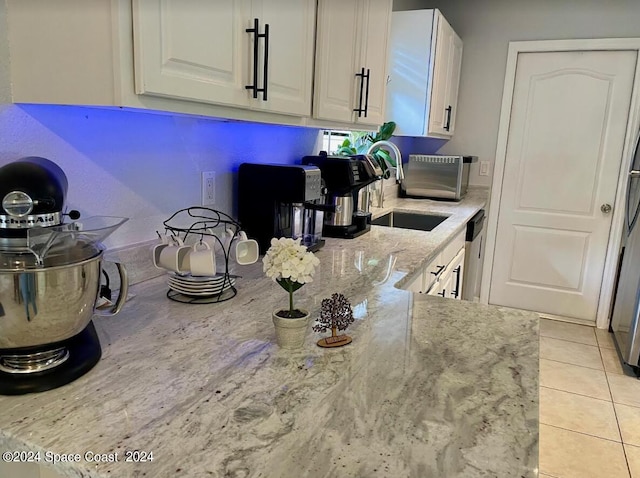 kitchen featuring light stone countertops, dishwasher, sink, white cabinetry, and light tile patterned floors