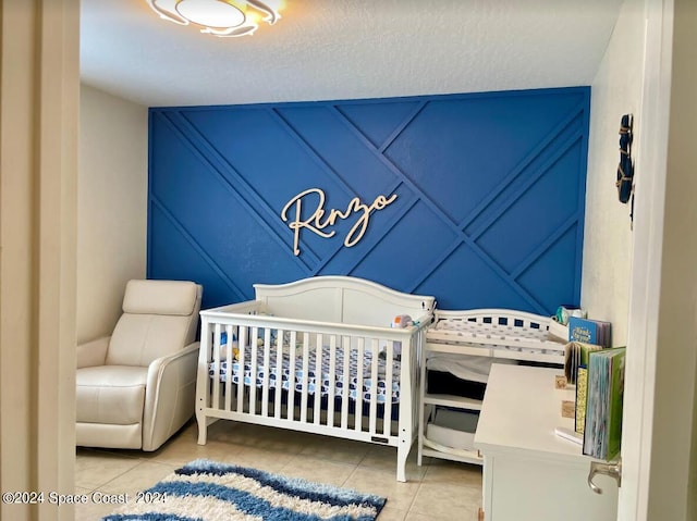 bedroom with a textured ceiling, a crib, and light tile patterned floors