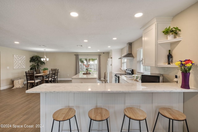 kitchen featuring wood-type flooring, kitchen peninsula, white cabinetry, wall chimney exhaust hood, and stainless steel electric range oven