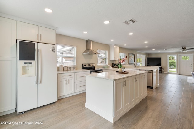 kitchen featuring wall chimney exhaust hood, white cabinetry, stainless steel appliances, and a wealth of natural light