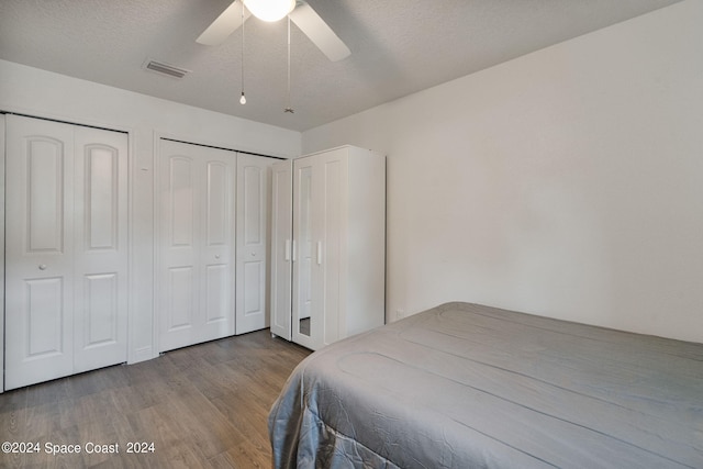 bedroom featuring light hardwood / wood-style floors, a textured ceiling, two closets, and ceiling fan