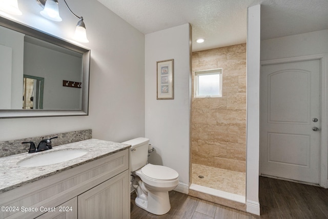 bathroom with a tile shower, wood-type flooring, a textured ceiling, toilet, and vanity